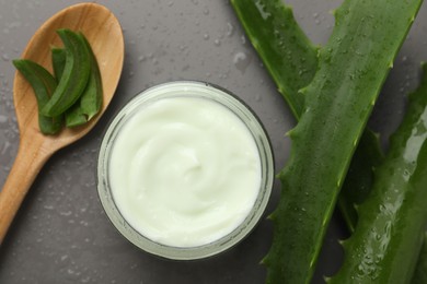 Photo of Moisturizing cream with extract of aloe vera in jar, cut leaves, spoon and water drops on grey background, flat lay