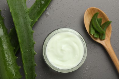 Photo of Moisturizing cream with extract of aloe vera in jar, cut leaves, spoon and water drops on grey background, flat lay