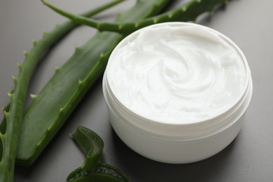 Photo of Moisturizing cream with extract of aloe vera in jar and cut leaves on grey background, closeup