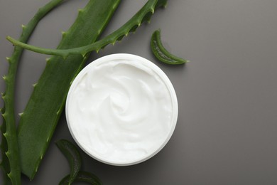 Photo of Moisturizing cream with extract of aloe vera in jar and cut leaves on grey background, flat lay. Space for text