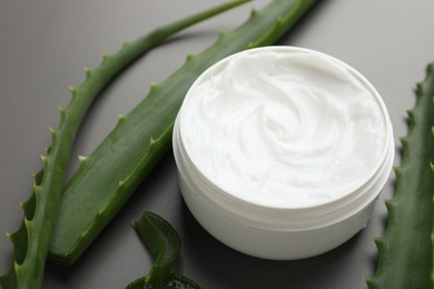 Photo of Moisturizing cream with extract of aloe vera in jar and cut leaves on grey background, closeup