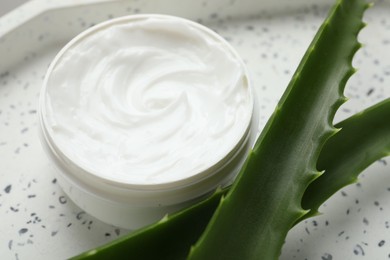 Photo of Moisturizing cream with extract of aloe vera in jar and cut leaves on white plate, closeup