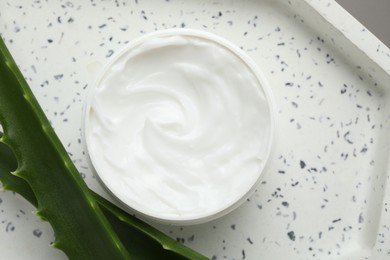 Photo of Moisturizing cream with extract of aloe vera in jar and cut leaves on white plate, top view