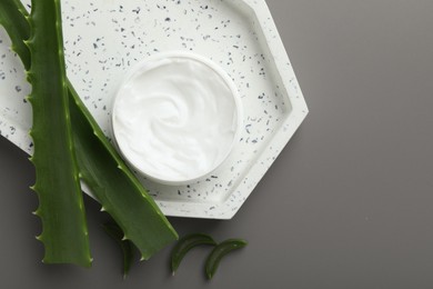 Photo of Moisturizing cream with extract of aloe vera in jar and cut leaves on grey background, flat lay. Space for text