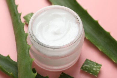 Photo of Moisturizing cream with extract of aloe vera in jar and cut leaves on pink background, closeup