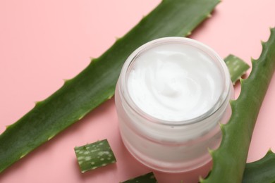 Photo of Moisturizing cream with extract of aloe vera in jar and cut leaves on pink background, closeup