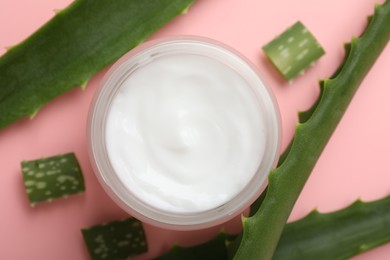 Moisturizing cream with extract of aloe vera in jar and cut leaves on pink background, flat lay