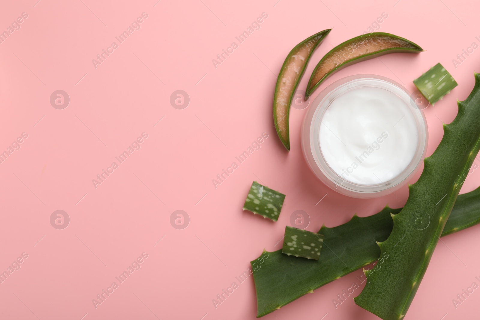 Photo of Moisturizing cream with extract of aloe vera in jar and cut leaves on pink background, flat lay. Space for text