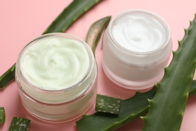 Photo of Moisturizing cream with extract of aloe vera and cut leaves on pink background, closeup