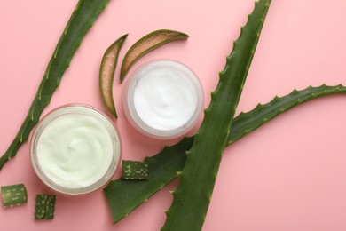 Photo of Moisturizing cream with extract of aloe vera and cut leaves on pink background, flat lay