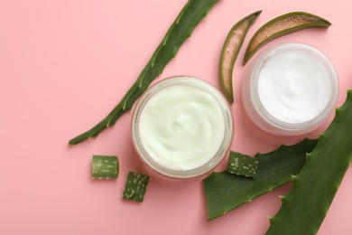 Moisturizing cream with extract of aloe vera and cut leaves on pink background, flat lay