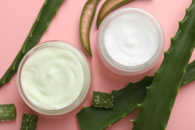 Photo of Moisturizing cream with extract of aloe vera and cut leaves on pink background, flat lay