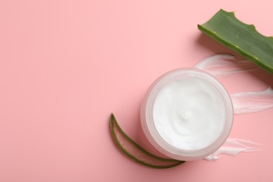 Moisturizing cream with extract of aloe vera in jar and cut leaves on pink background, flat lay. Space for text