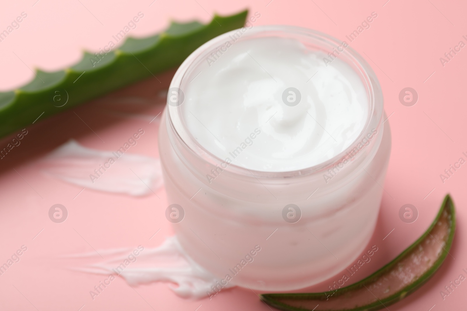 Photo of Moisturizing cream with extract of aloe vera in jar and cut leaves on pink background, closeup