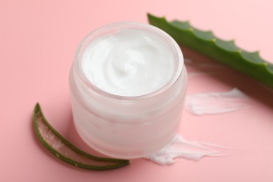 Photo of Moisturizing cream with extract of aloe vera in jar and cut leaves on pink background, closeup