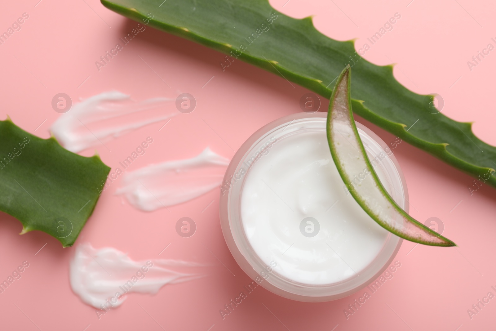 Photo of Moisturizing cream with extract of aloe vera in jar and cut leaves on pink background, flat lay