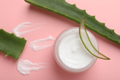 Moisturizing cream with extract of aloe vera in jar and cut leaves on pink background, flat lay