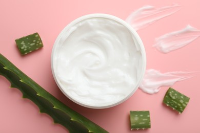 Moisturizing cream with extract of aloe vera in jar and cut leaves on pink background, flat lay