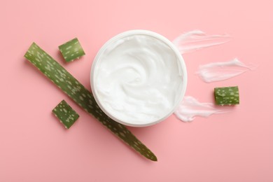 Photo of Moisturizing cream with extract of aloe vera in jar and cut leaves on pink background, flat lay