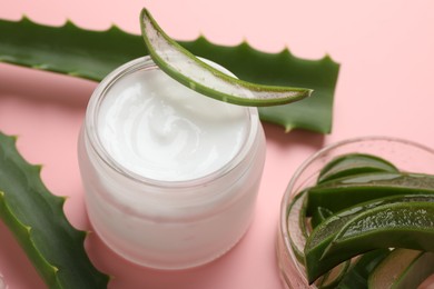 Moisturizing cream with extract of aloe vera in jar and cut leaves on pink background, closeup