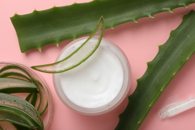 Photo of Moisturizing cream with extract of aloe vera in jar and cut leaves on pink background, flat lay