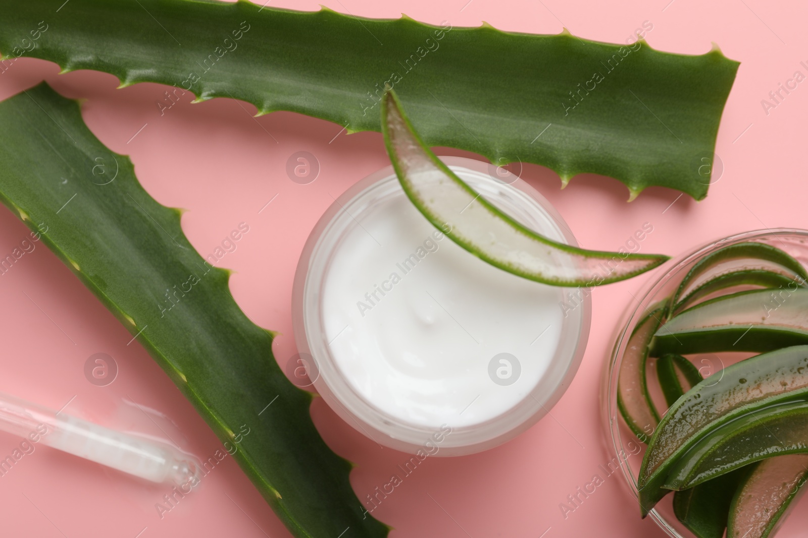 Photo of Moisturizing cream with extract of aloe vera in jar and cut leaves on pink background, flat lay