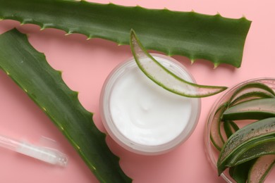 Moisturizing cream with extract of aloe vera in jar and cut leaves on pink background, flat lay