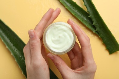 Photo of Woman with moisturizing cream and wet aloe vera leaves on yellow background, top view