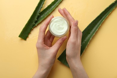 Woman with moisturizing cream and wet aloe vera leaves on yellow background, top view