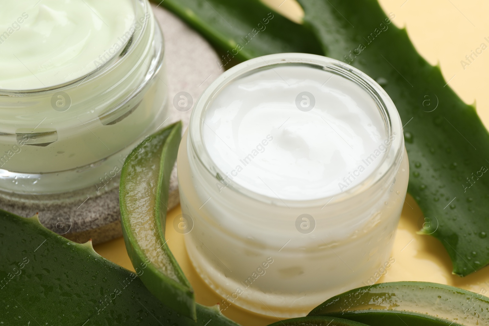 Photo of Moisturizing cream with extract of aloe vera and cut leaves on yellow background, closeup