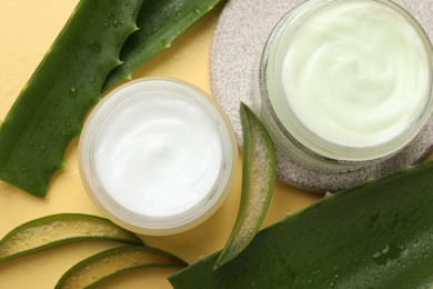 Photo of Moisturizing cream with extract of aloe vera and cut leaves on yellow background, flat lay