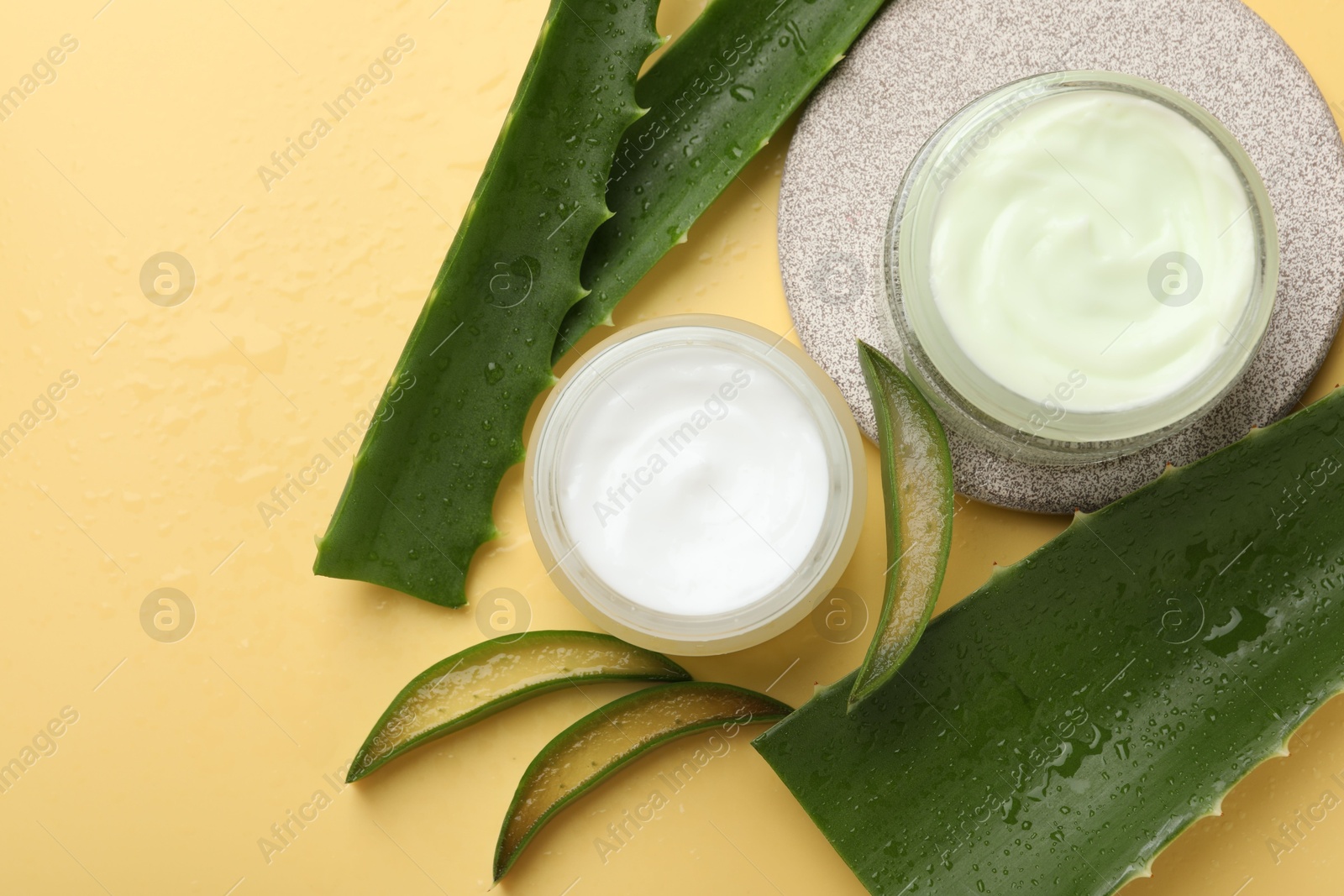 Photo of Moisturizing cream with extract of aloe vera and cut leaves on yellow background, flat lay