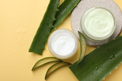 Photo of Moisturizing cream with extract of aloe vera and cut leaves on yellow background, flat lay