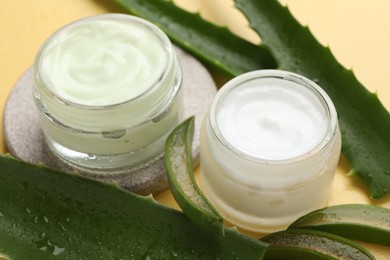 Photo of Moisturizing cream with extract of aloe vera and cut leaves on yellow background, closeup