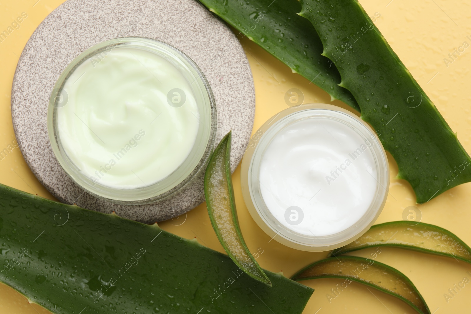 Photo of Moisturizing cream with extract of aloe vera and cut leaves on yellow background, flat lay