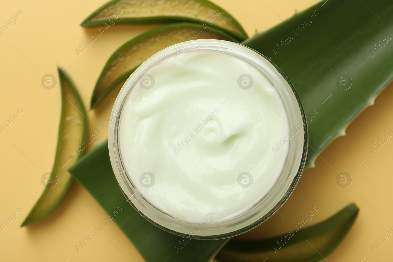 Photo of Moisturizing cream with extract of aloe vera in jar and cut leaves on yellow background, flat lay