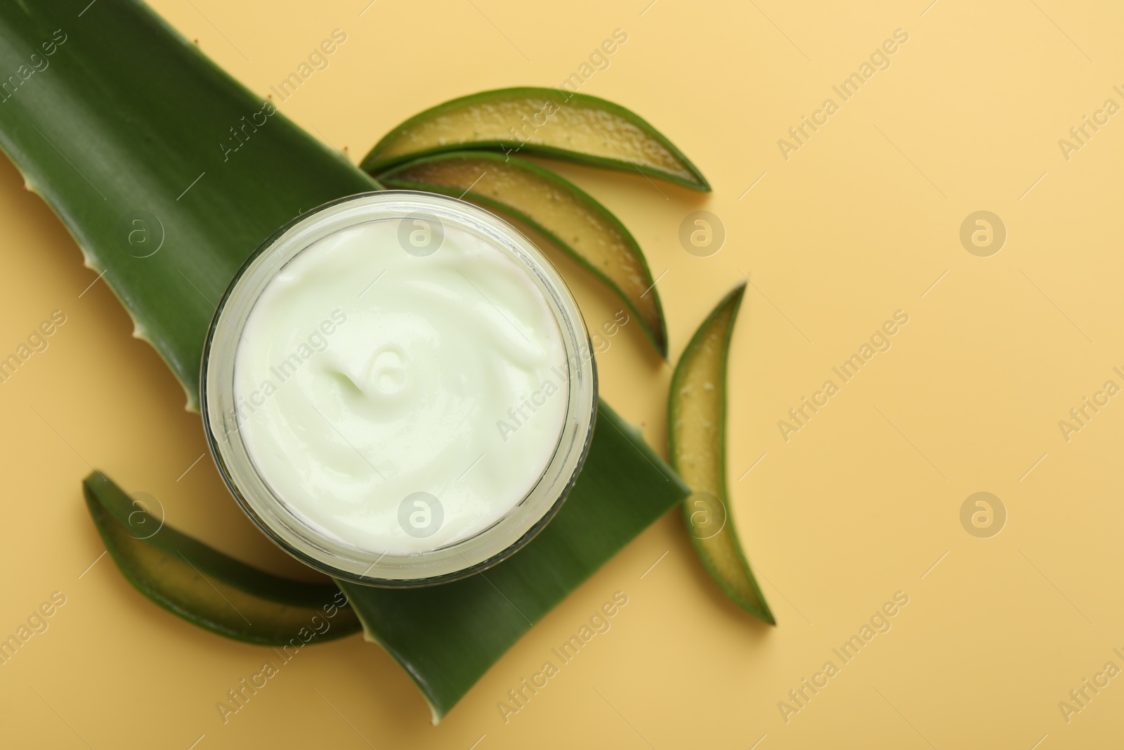 Photo of Moisturizing cream with extract of aloe vera in jar and cut leaves on yellow background, flat lay. Space for text