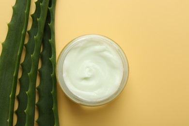 Photo of Moisturizing cream with extract of aloe vera in jar and cut leaves on yellow background, flat lay. Space for text