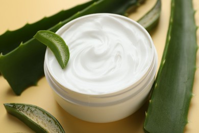 Moisturizing cream with extract of aloe vera in jar and cut leaves on yellow background, closeup