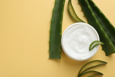 Photo of Moisturizing cream with extract of aloe vera in jar and cut leaves on yellow background, flat lay. Space for text