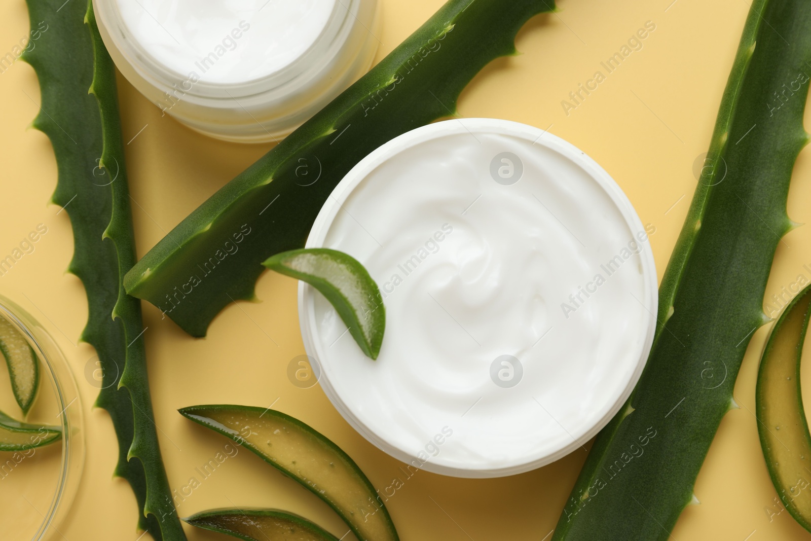 Photo of Moisturizing cream with extract of aloe vera and cut leaves on yellow background, flat lay