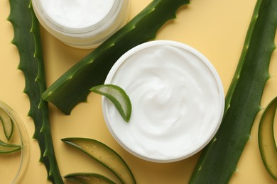 Moisturizing cream with extract of aloe vera and cut leaves on yellow background, flat lay