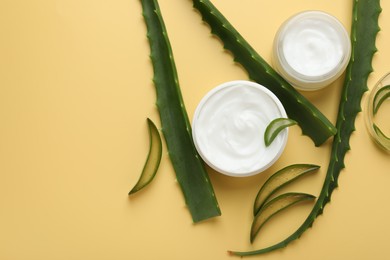 Photo of Moisturizing cream with extract of aloe vera and cut leaves on yellow background, flat lay. Space for text