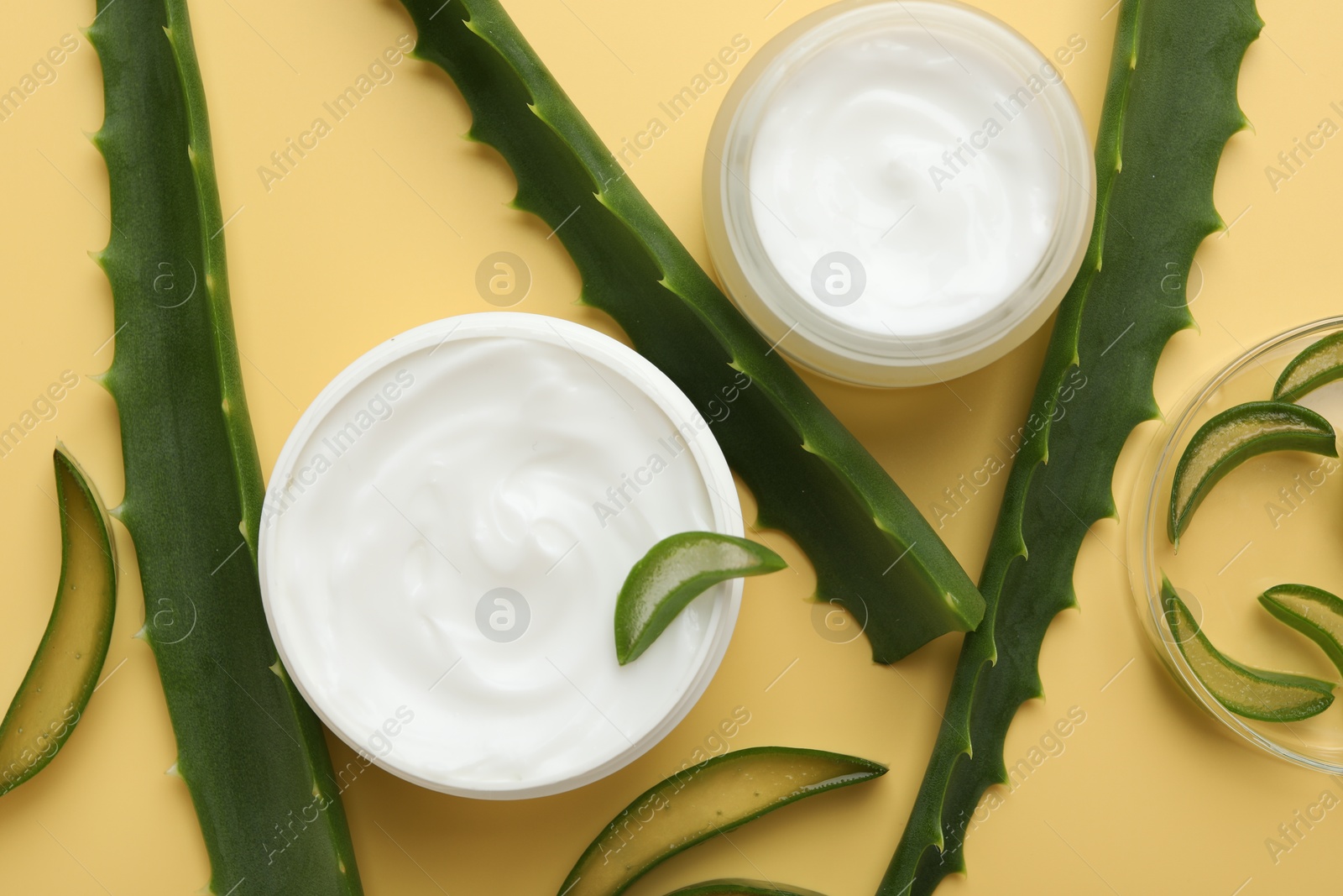 Photo of Moisturizing cream with extract of aloe vera and cut leaves on yellow background, flat lay