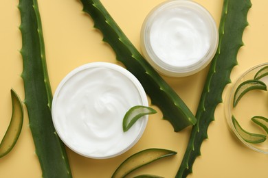 Moisturizing cream with extract of aloe vera and cut leaves on yellow background, flat lay