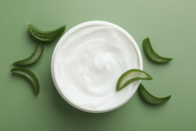 Photo of Moisturizing cream with extract of aloe vera in jar and cut leaves on green background, flat lay