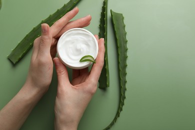 Photo of Woman with moisturizing cream and aloe vera leaves on green background, top view. Space for text