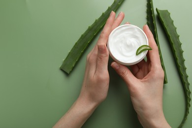 Woman with moisturizing cream and aloe vera leaves on green background, top view. Space for text