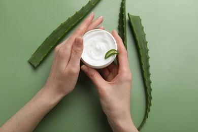 Woman with moisturizing cream and aloe vera leaves on green background, top view