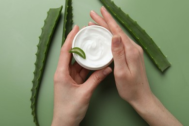 Woman with moisturizing cream and aloe vera leaves on green background, top view